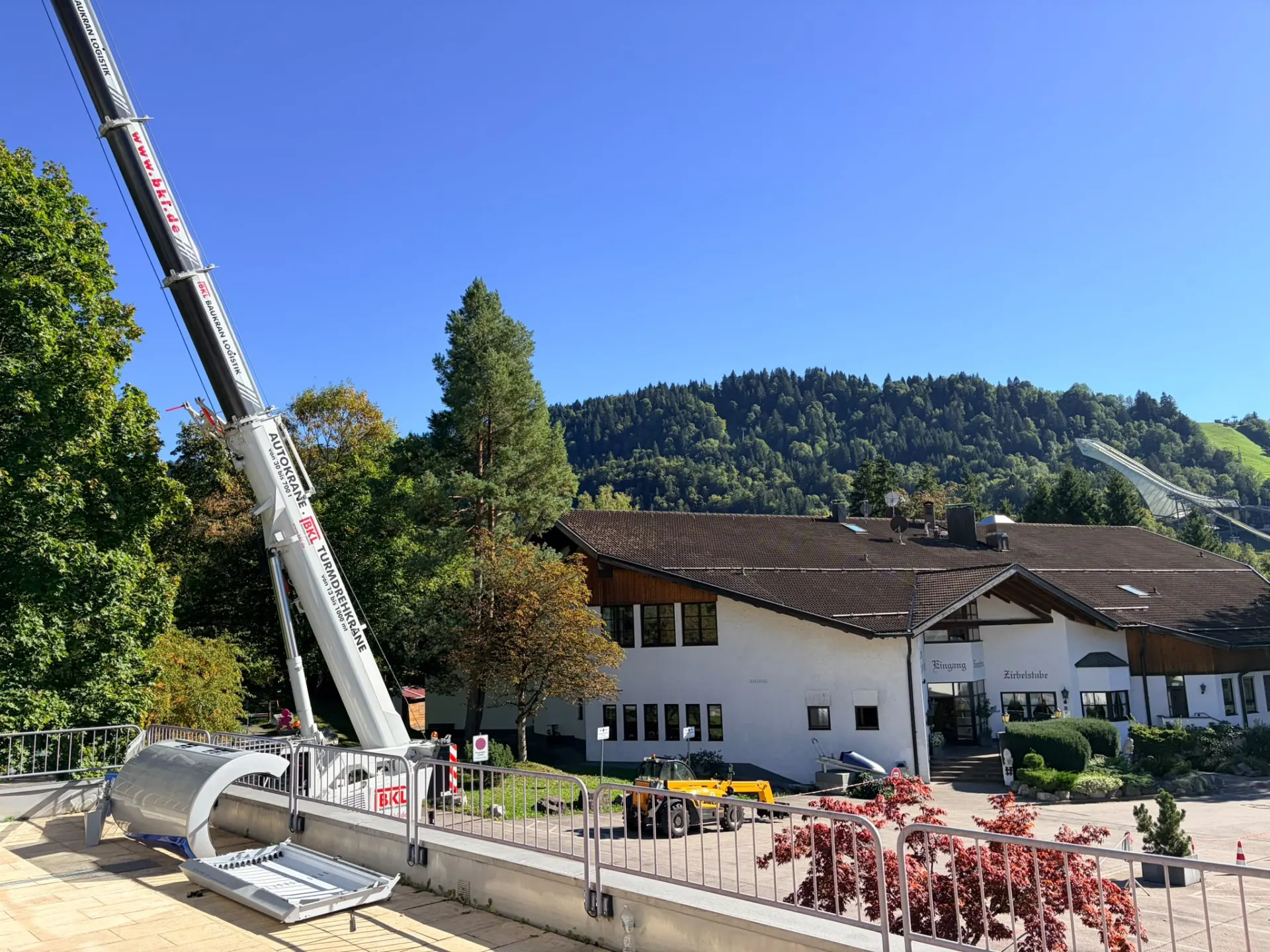 Autokran setzt Material auf der Terrasse vor der Halle ab